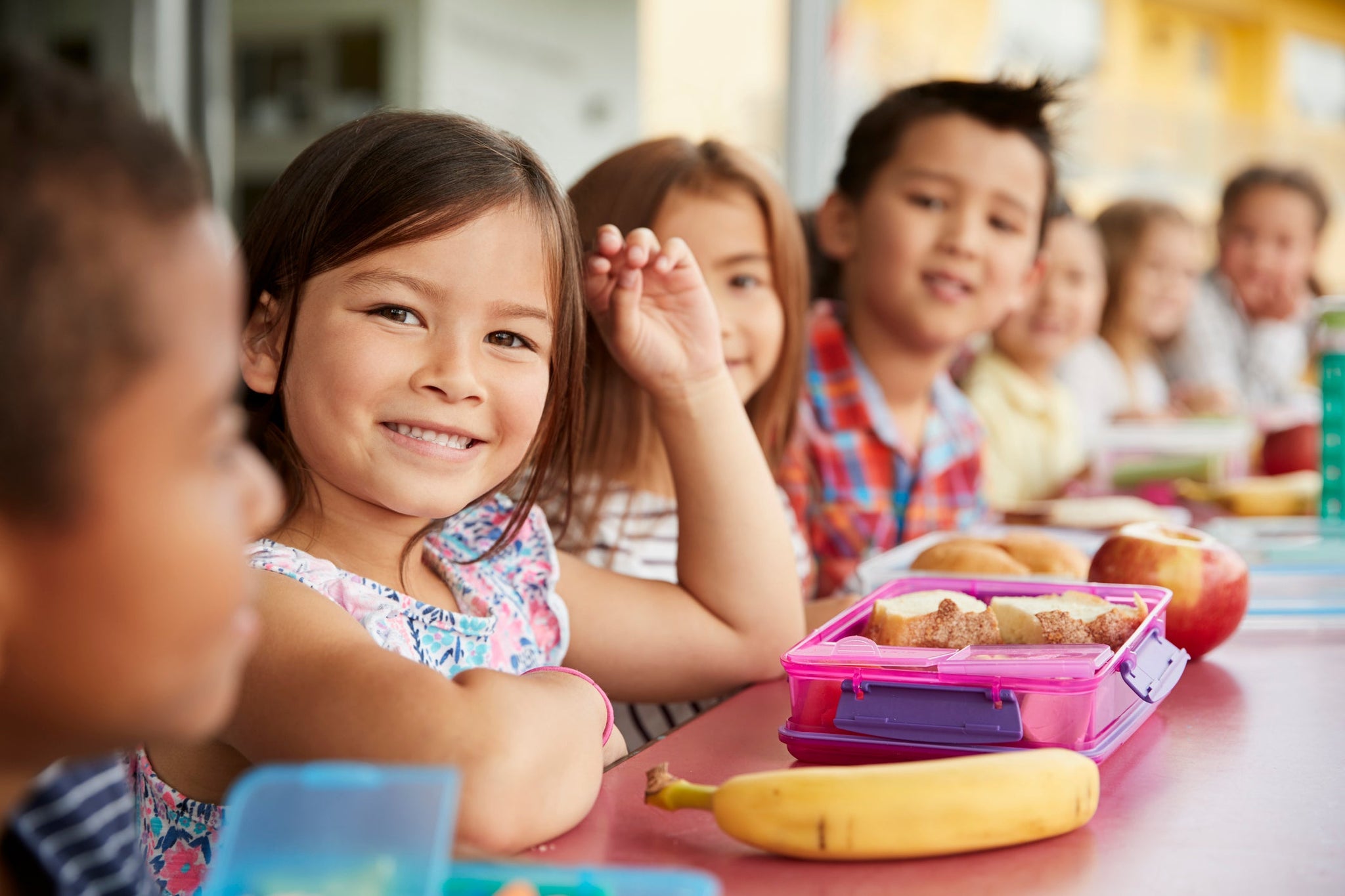 Group of school aged children sitting at a table with smiles and healthy food